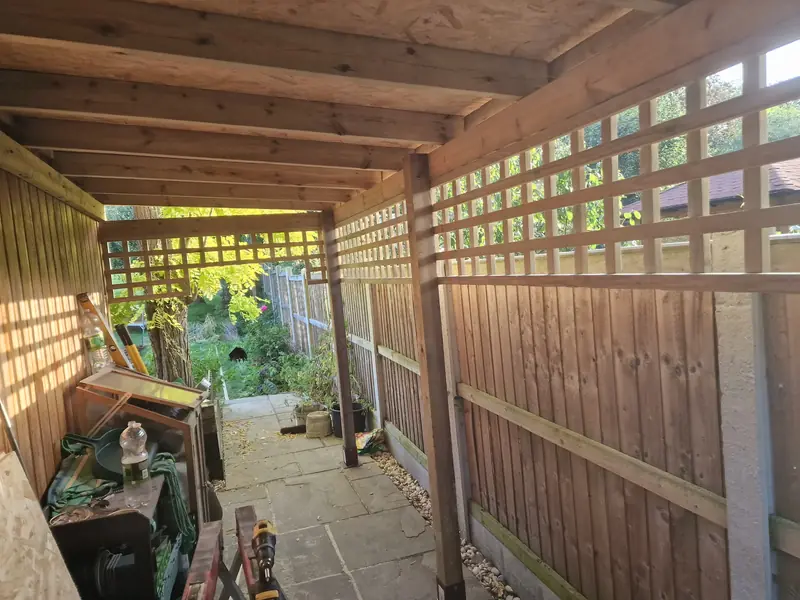 Timber canopy over a side passage with trellis screening, close-board fencing and stone paving in Lexden