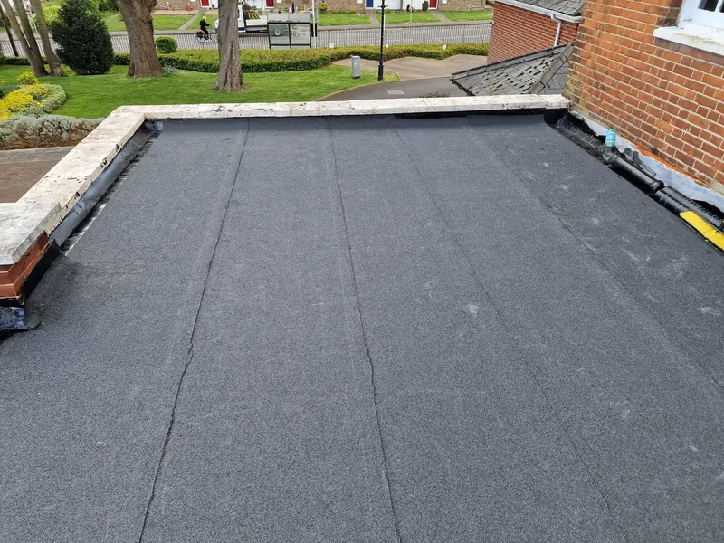 Newly finished mineral felt flat roof with stone coping on the edge, beside a brick wall in Witham