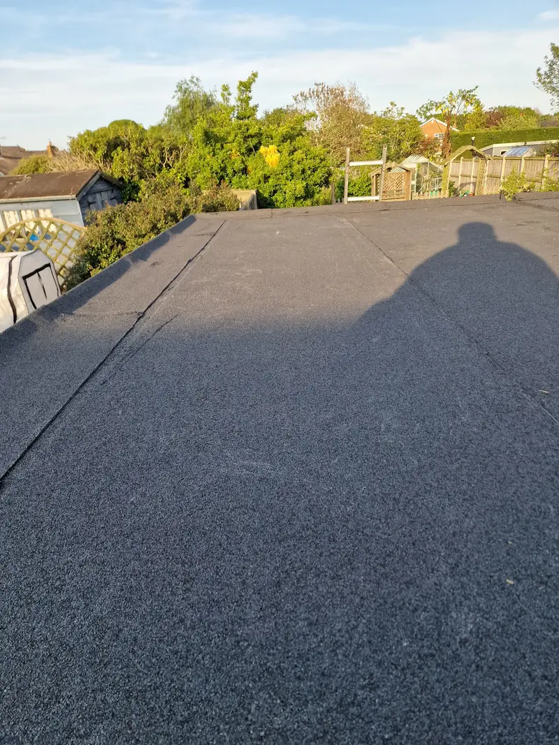 Newly laid mineral felt flat roof with neat lapped joints, looking out over neighbouring gardens