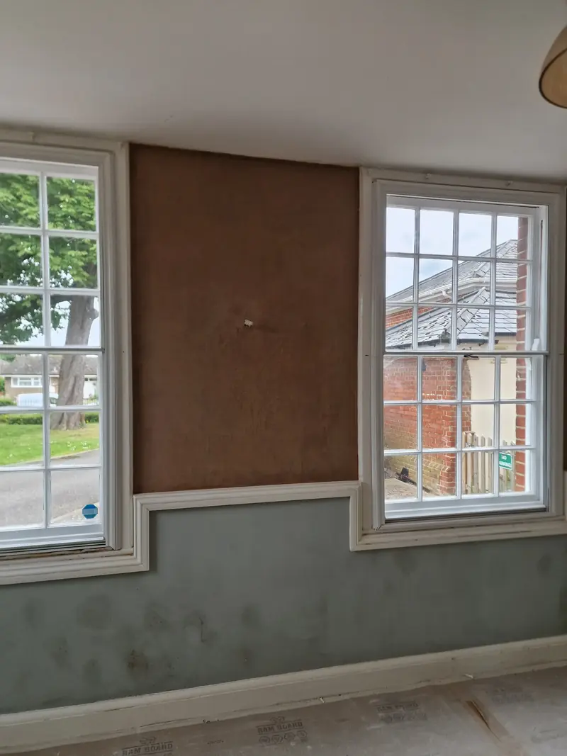 Two sash windows with a boarded wall section between them and marked grey-green paintwork below