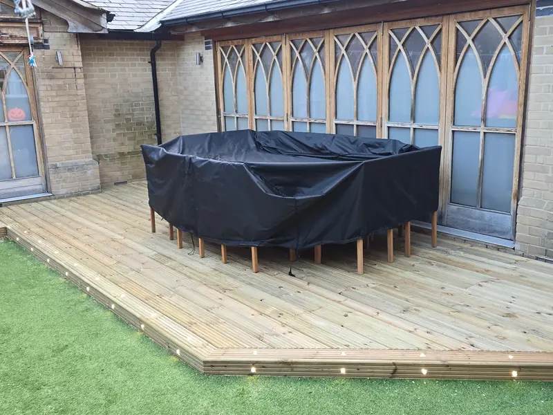 Second view of the Colchester deck with inset lights along the edge, set on artificial grass beside arched windows