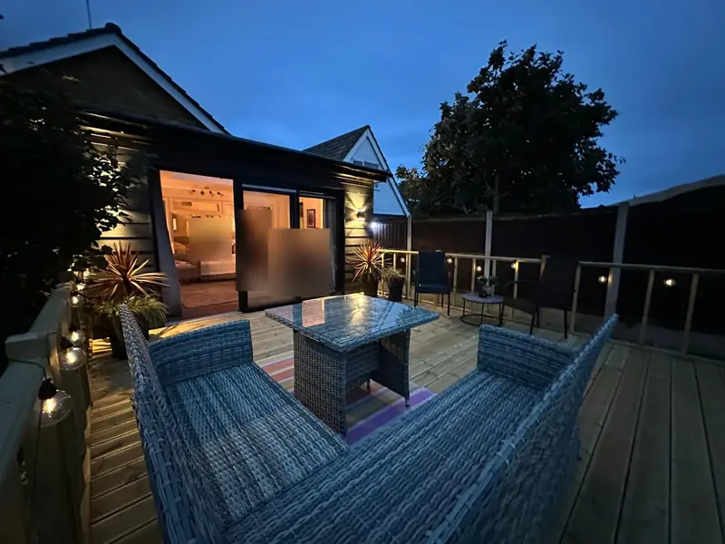 The Clacton-on-Sea deck at dusk with festoon lights, rattan garden furniture and glazed doors into the house