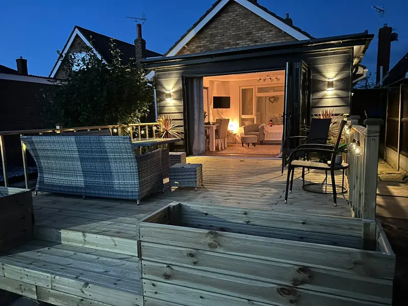 The Clacton-on-Sea deck at dusk with planters, rattan seating and wall lights, bi-fold doors open behind