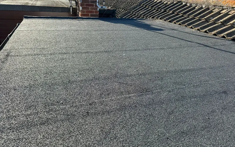 Finished felt flat roof with a brick chimney stack beyond, next to a concrete-tiled pitched roof in Rowhedge