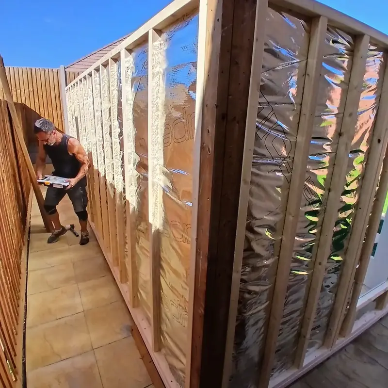 Close view of a timber stud wall filled with foil-faced insulation, with an installer working along the side path.