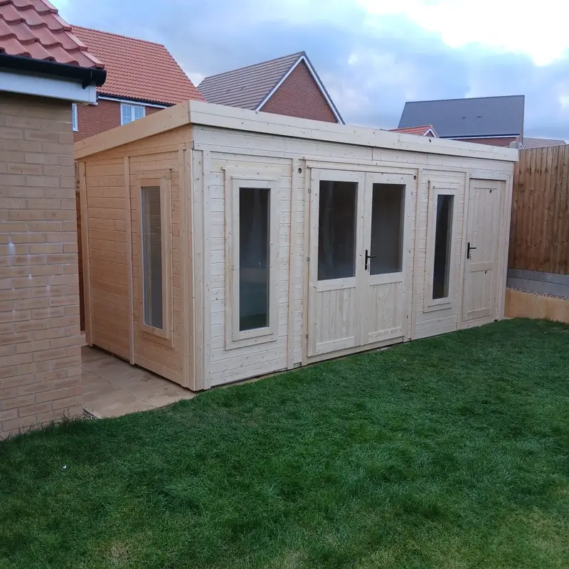 Finished pent timber garden building with glazed double doors, two tall windows and a store door, on a lawn by a brick wall